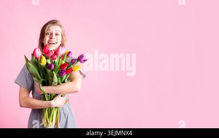 Happy young woman holding bouquet of fresh tulips isolated on pink background Stock Photo