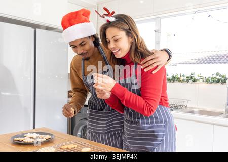 Couple standing at kitchen countertop wearing matching aprons, decorating cookies with piping tool. Baking, desserts, festive, cozy, romantic, duo, ho Stock Photo