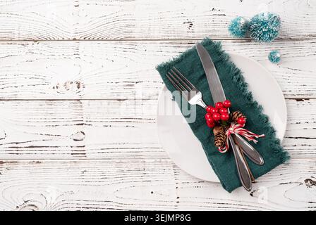 Christmas table setting with white dishware, silverware and red and green decorations on white wooden background. Top view. Stock Photo