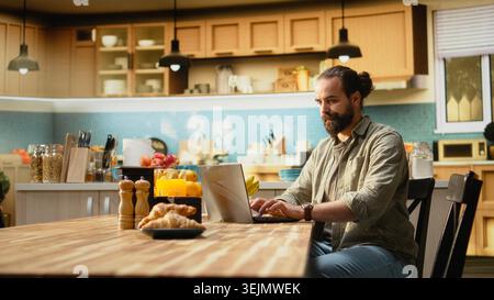 Adult worker checking time on wristwatch and running late to the office, preparing to leave home in a hurry and avoid delay. Male looking at the late hour during breakfast in kitchen. Stock Photo