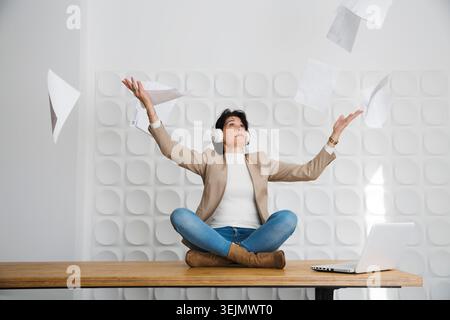 Tired angry businesswoman touching head with laptop, she sits on a table and throwing up paper account documents Stock Photo