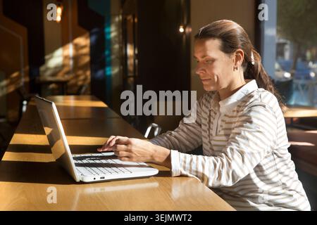 Work from vacation home, remote workers. middle aged woman using a laptop, connecting to the Internet and talking on a cell phon Stock Photo