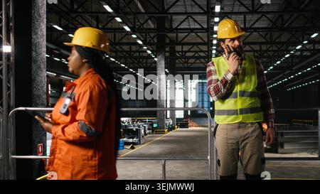Professional engineer using walkie-talkie inside heavy industry facility, coordinating the production line with portable radio transceiver. Machinery hall with two-way communication. Stock Photo