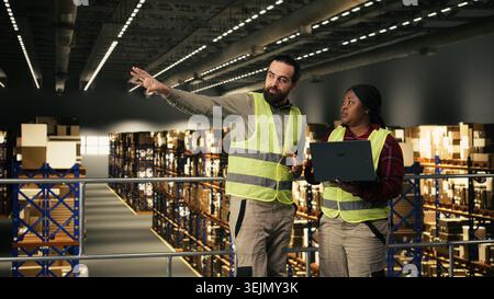 Multicultural team collaborating in industrial warehouse on platform, two workers coordinate parcel handling and shipping workflow. Supply chain control to ensure e-commerce operations. Stock Photo