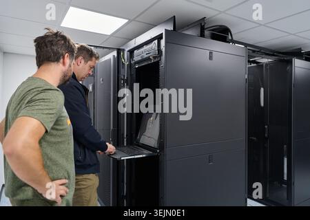 Two IT technicians working on a server rack in a modern data center troubleshooting network hardware Stock Photo