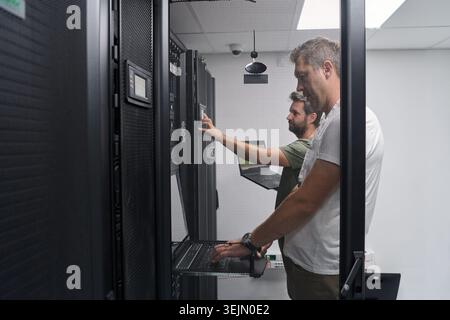 Two IT technicians working on servers in a data center performing network maintenance and system checks Stock Photo