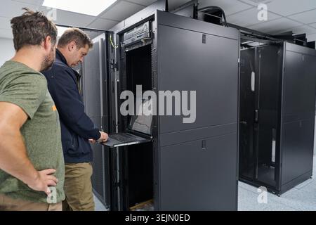 Two IT technicians working on a server rack with a laptop in a modern data center Stock Photo