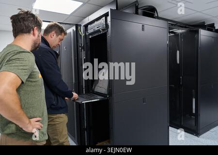 Data center technicians troubleshoot rack-mounted servers using a pull-out console laptop during maintenance Stock Photo