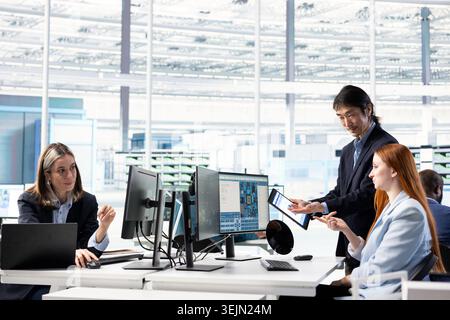 Working together, computer monitor and multiracial team designing complex PCB layout. Optimizing integrated circuit production, development phase and teamworking colleagues using specialized software Stock Photo