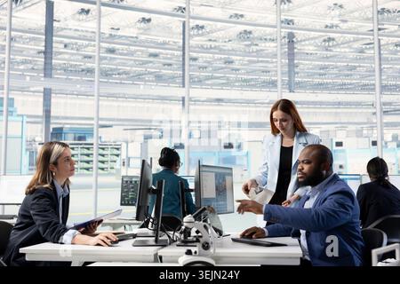 Female semiconductor engineer and colleague brainstorm SoC architecture design in hardware manufacturing facility office. Woman and African american man in RD workspace research microelectronic parts Stock Photo