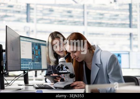 Engineering team analyzing nanotechnology circuits with microscope in microchip factory RD office, brainstorming. Teamworking colleagues inspect PCB parts with optical gear in research facility Stock Photo