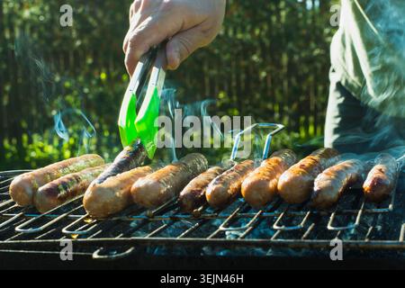 Male hand turned the sausages over open fire barbecue. Close up. Outdoor. Stock Photo