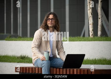 Man Using Laptop on Outdoor Bench for Remote Work Stock Photo