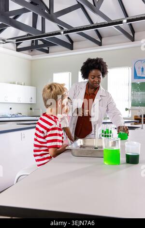 African American instructor wearing white lab coat teaching two children in school lab with beakers. Classroom, science, glasswa Stock Photo
