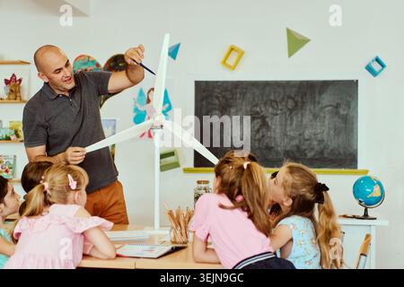 Teacher demonstrating model wind turbine to elementary students during hands-on STEM lesson in classroom Stock Photo