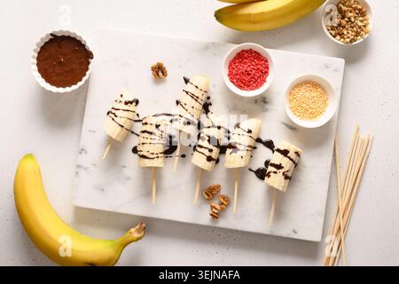 Cooking homemade banana lollipops with different sprinkles on white. Stock Photo