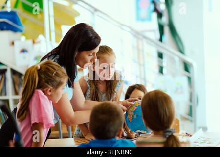 A teacher guides a small group of engaged primary students as they explore a colorful globe, fostering curiosity, teamwork and hands-on learning in a Stock Photo
