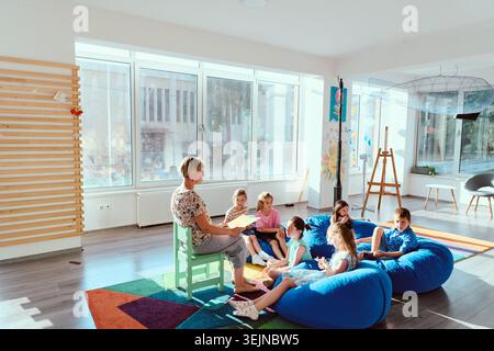 Teacher reading to a group of children on beanbags in a bright modern classroom during storytime Stock Photo