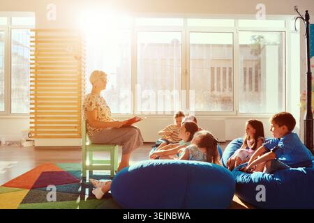 Teacher reading a story to children during storytime in a bright sunny classroom Stock Photo