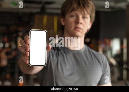Young sporty man showing white blank screen mockup cellphone in gym Stock Photo