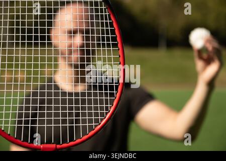 Man looking through badminton racket on floor sport badminton court. Outdoors. Close up. Stock Photo