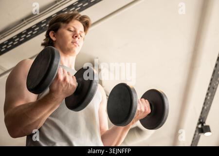 Young man doing dumbbell biceps curl in fitness club Stock Photo