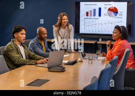 Diverse coworkers collaborating at conference room with leader in blazer using laptops and monitor. Collaboration, teamwork, pre Stock Photo