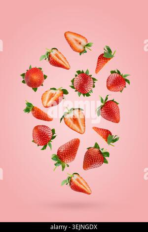 Ripe strawberry slices and whole with luscious red texture, green leaves soar as flow on pink background. Perfect for vegetarian Stock Photo