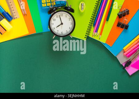 Colorful school supplies, book, and alarm clock on green. Stock Photo