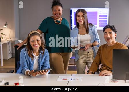 Coworkers gathering in meeting room reviewing slide while using tablet laptop smartphone and charts. Colleagues, teamwork, collaboration, office, conf Stock Photo