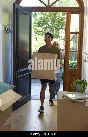 Diverse household members carrying moving boxes and entering entryway with wooden door, plants. Relocation, cardboard, packing, couple, foyer, thresho Stock Photo