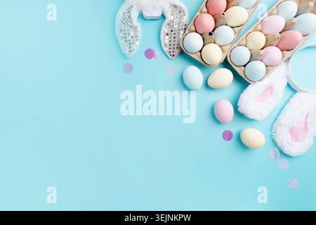 Pastel colored Easter eggs and bunny ears on blue background with copy space Stock Photo