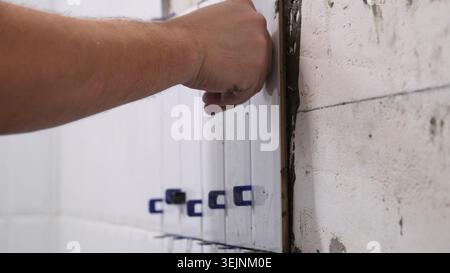 The hands of the tiler are laying the ceramic tile on the wall Stock Photo