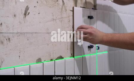 The hands of the tiler are laying the ceramic tile on the wall Stock Photo
