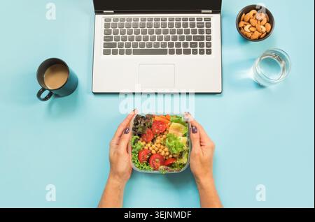 Healthy business lunch in the office, salad for snack, glass of water, almonds, cup of coffee on blue. Top view with copy space. Stock Photo