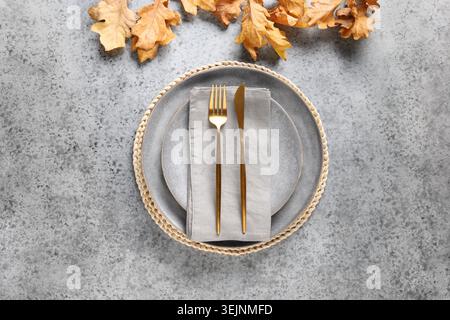 Autumn table setting decorated dry oak leaf and golden cutlery on gray table. Stock Photo