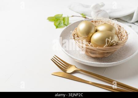 Easter table setting with bunny and golden eggs on white table. Close up. Stock Photo