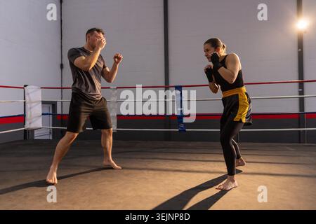 Male and female training partners sparring in boxing ring at gym wearing sportswear and hand wraps. Athlete, barefoot, combat, f Stock Photo