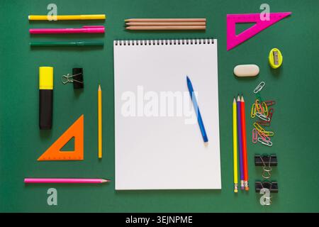 Colorful school supplies, book, and alarm clock on green. Stock Photo