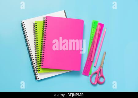 Colorful girlish school supplies, notebooks and pens on blue. Stock Photo