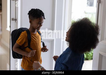 Mother and son smiling and talking at front door, boy wearing backpack and orange T-shirt. Family, parent, child, home, hallway, Stock Photo