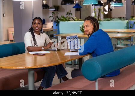 Coworkers collaborating, reviewing charts on laptops in coworking lounge with papers and smartphone. Business, teamwork, collaboration, office, worksp Stock Photo