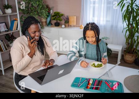 Mother talking on phone and using laptop while daughter studying Stock Photo