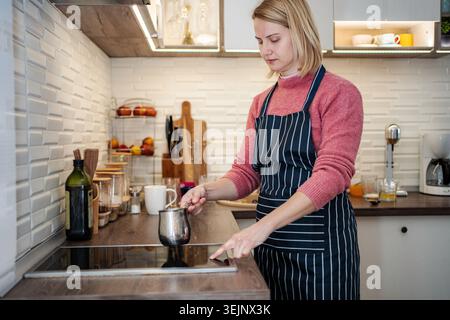 Woman making coffee on induction stove in kitchen Stock Photo