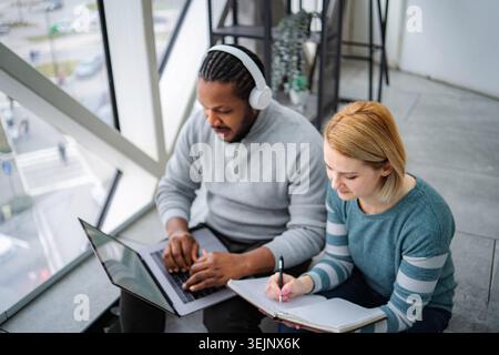 Diverse students collaborating on study project using laptop and notebook Stock Photo