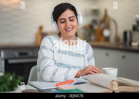 Young woman studying at home wearing headphones and smiling Stock Photo