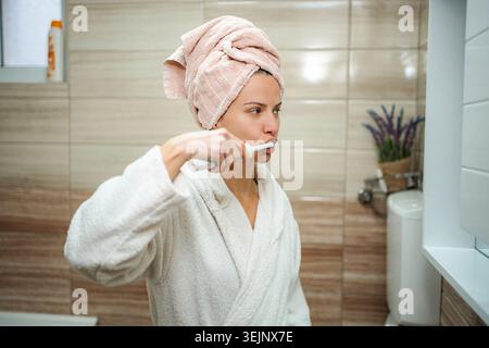 Woman brushing teeth with electric toothbrush in bathroom Stock Photo