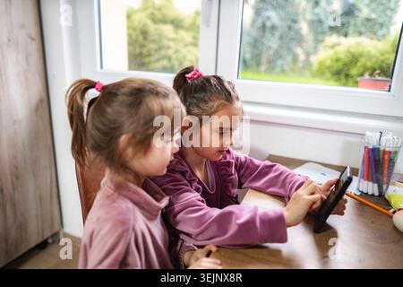 Sisters learning at home using digital tablet technology Stock Photo