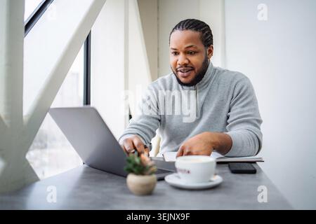Young black man working remotely on laptop in cafe Stock Photo