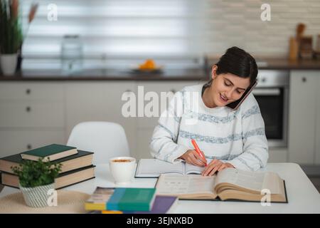 Young woman studying at home making phone call Stock Photo